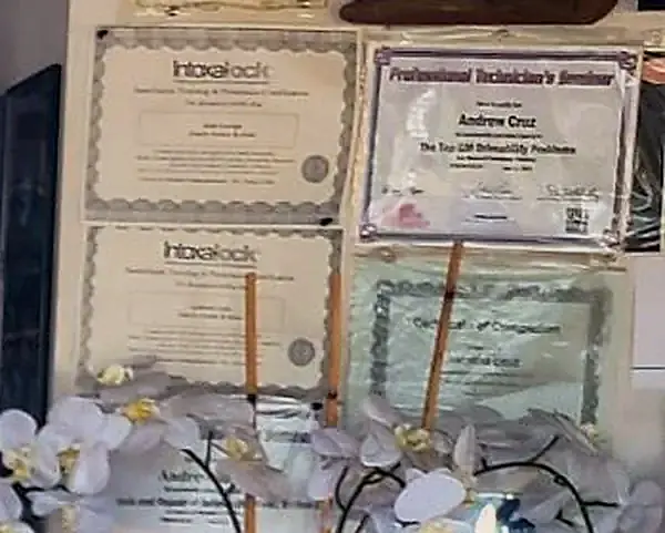 Andrew Cruz’s Professional Technician’s Seminar certificate on driveability problems, next to two Intoxalock technician training certificates on the office wall