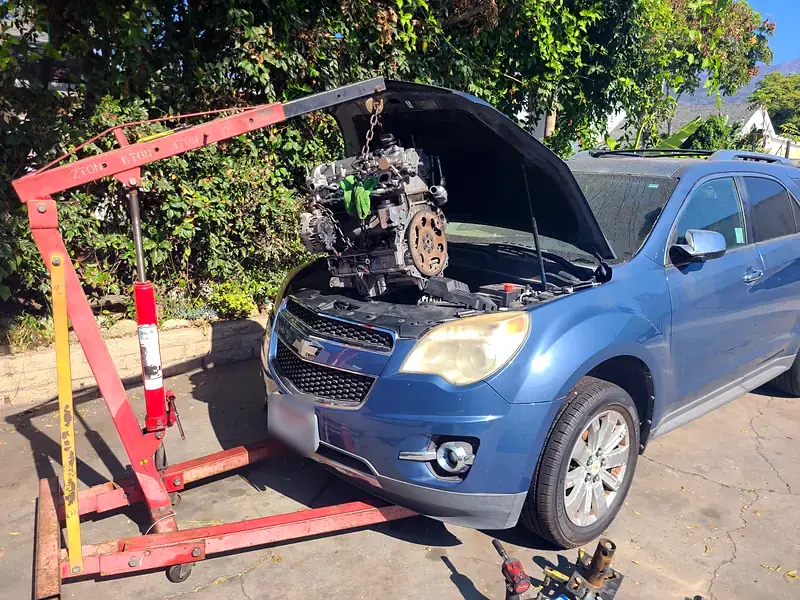 A Chevy Equinox with its engine out on the shop crane in the yard