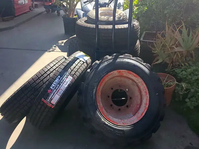 A stack of tires beside the tire machine at the shop, including a loader tire and new light-truck tires