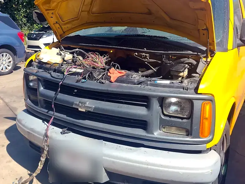 A yellow Chevy Express van with the hood up for electrical work at Beach Motor & Tires